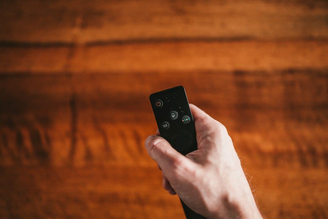 A hand holding a TV remote on a couch, ready to enter Moly IPTV Xtream Codes login details in an IPTV app